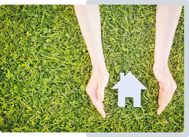 Protection du domicile grâce à un système d’alarme Mains protégeant une maison miniature sur une pelouse, symbolisant la sécurité et la protection du domicile.